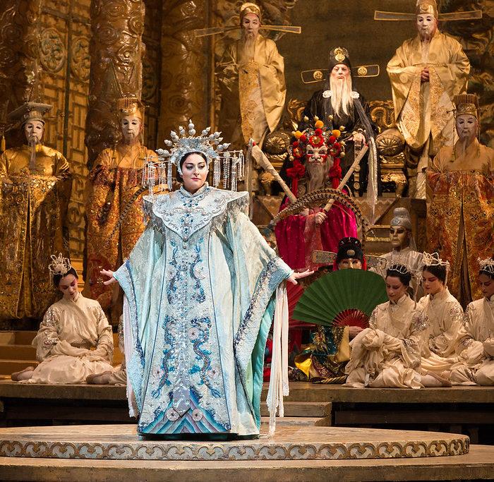 Opera singer performing on grand stage with dramatic lighting and audience